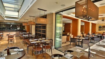 Um restaurante moderno com pé direito alto, grandes janelas e diversos tipos de assentos, incluindo mesas e cadeiras.