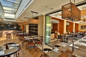 A modern restaurant with high ceilings, large windows, and a variety of seating arrangements including tables and chairs. - ALQasr Metropole Hotel (Amman)