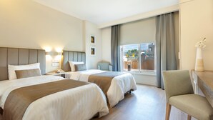 Hotellihuone, jossa on kaksi sänkyä, tuoli, työpöytä ja ikkuna, jossa on verhot.