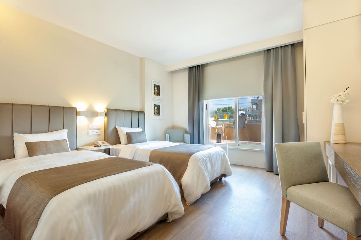 A hotel room with two beds, a chair, a desk, and a window with curtains.