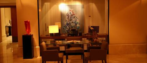 A modern hotel lobby with a glass table surrounded by chairs, a red sculpture, and a large abstract painting.