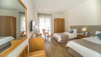 A hotel room with two beds, a desk with a mirror, a small table with a lamp, and a chair.