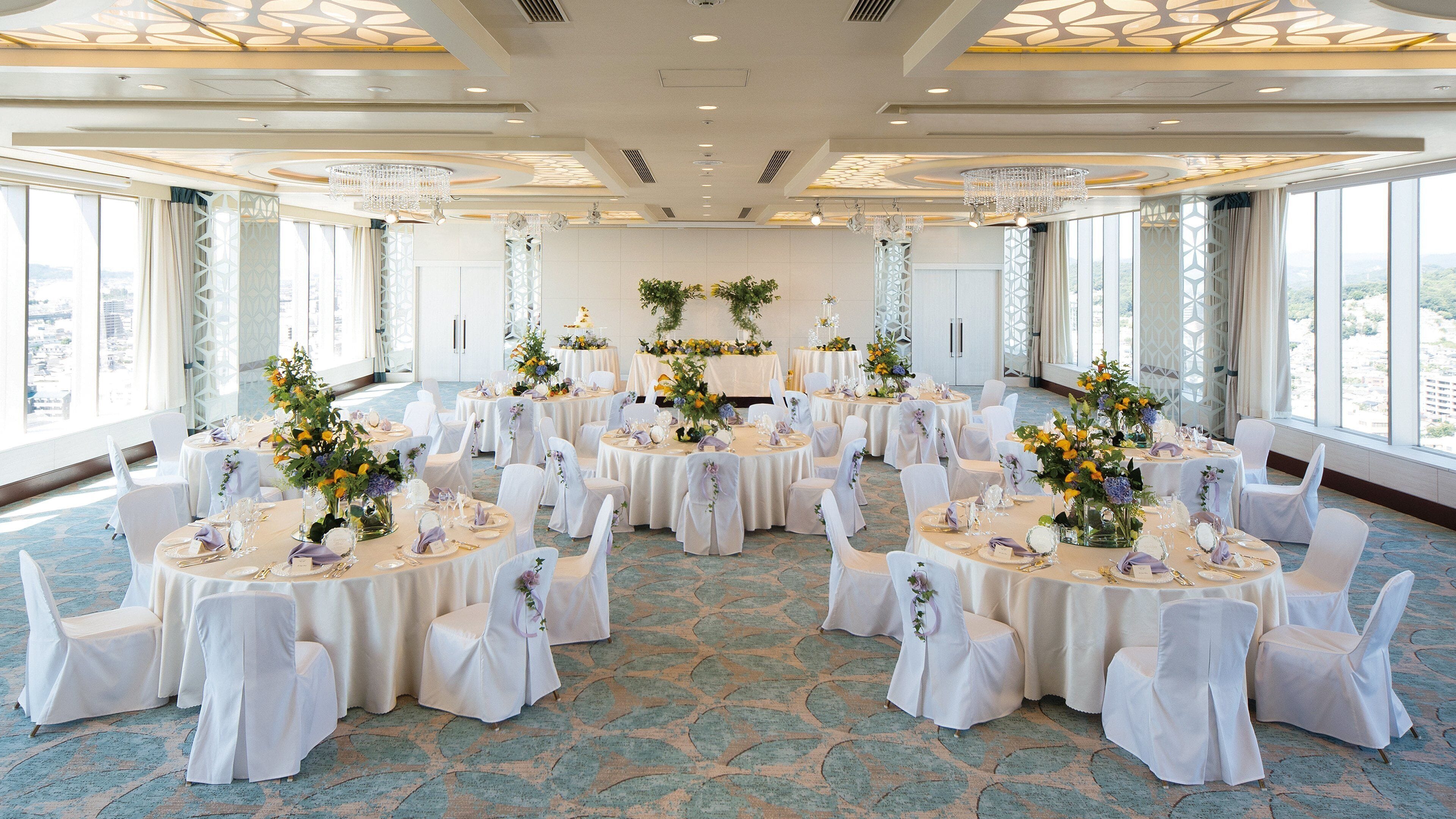 A banquet hall with round tables, white chairs, and floral centerpieces.