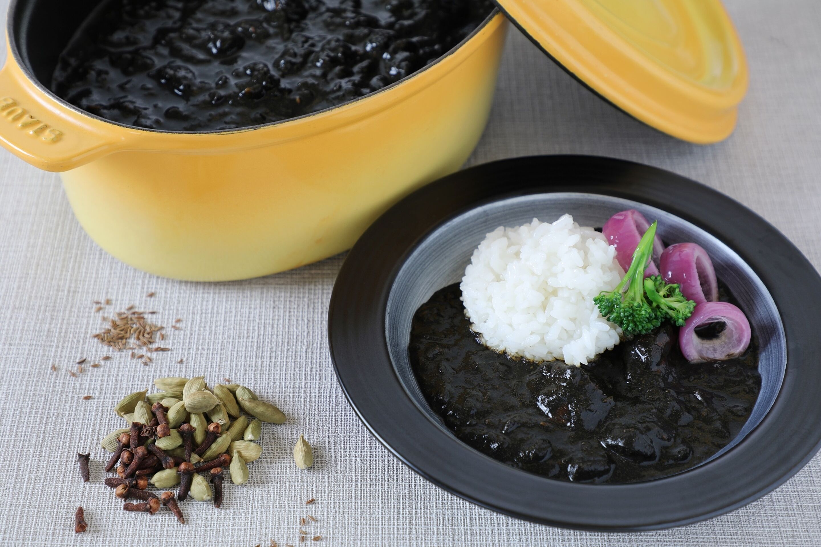 A bowl of black bean soup with rice and vegetables, a yellow pot, and scattered spices.