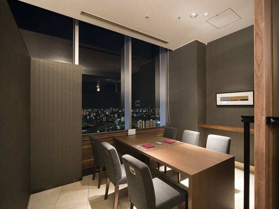 A conference room with a city view, large windows, and a long table with chairs.