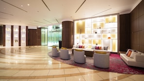 Een moderne lobby met een gebogen vloer, een zithoek met banken en poefs, en een wand met verlichte panelen.