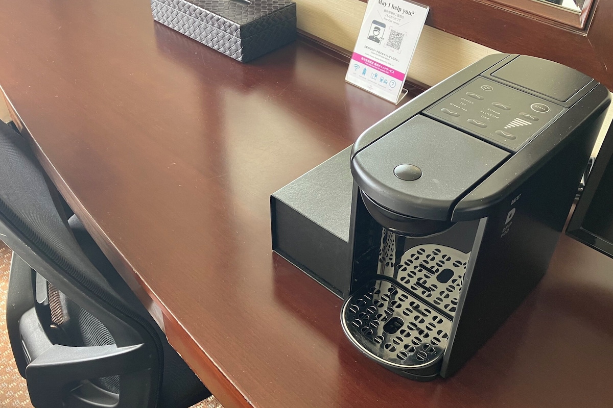 Una cafetera sobre una encimera de madera con un cartel de fondo.