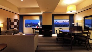 Habitación de hotel con sofá, una mesa de comedor con sillas, televisor y un ventanal con vista a la ciudad.