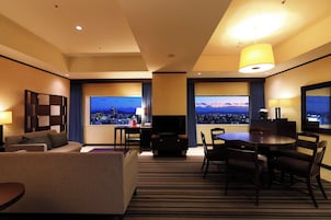 Habitación de hotel con vista a la ciudad, un sofá, una mesa de comedor y un televisor.