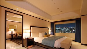 Habitación de hotel con cama, lámparas de noche, escritorio y vista a la ciudad de noche.