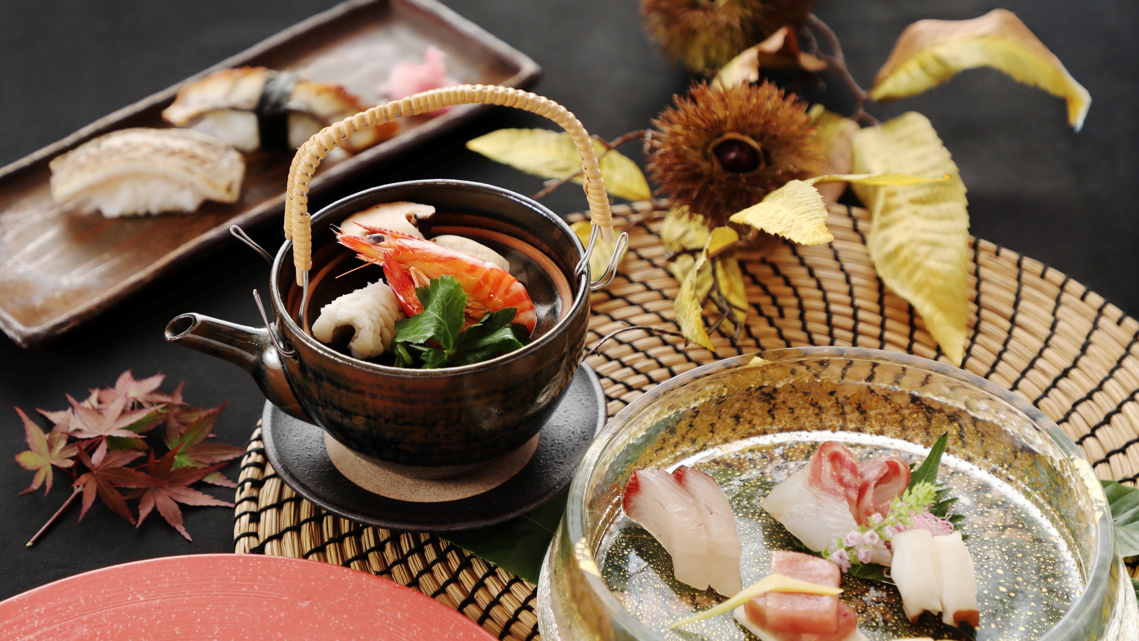 A traditional Japanese meal setup with a bowl of soup, sashimi, and sushi on a woven mat.