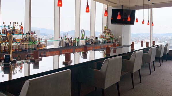 Un bar con una barra larga, varias sillas y una pantalla de televisión.