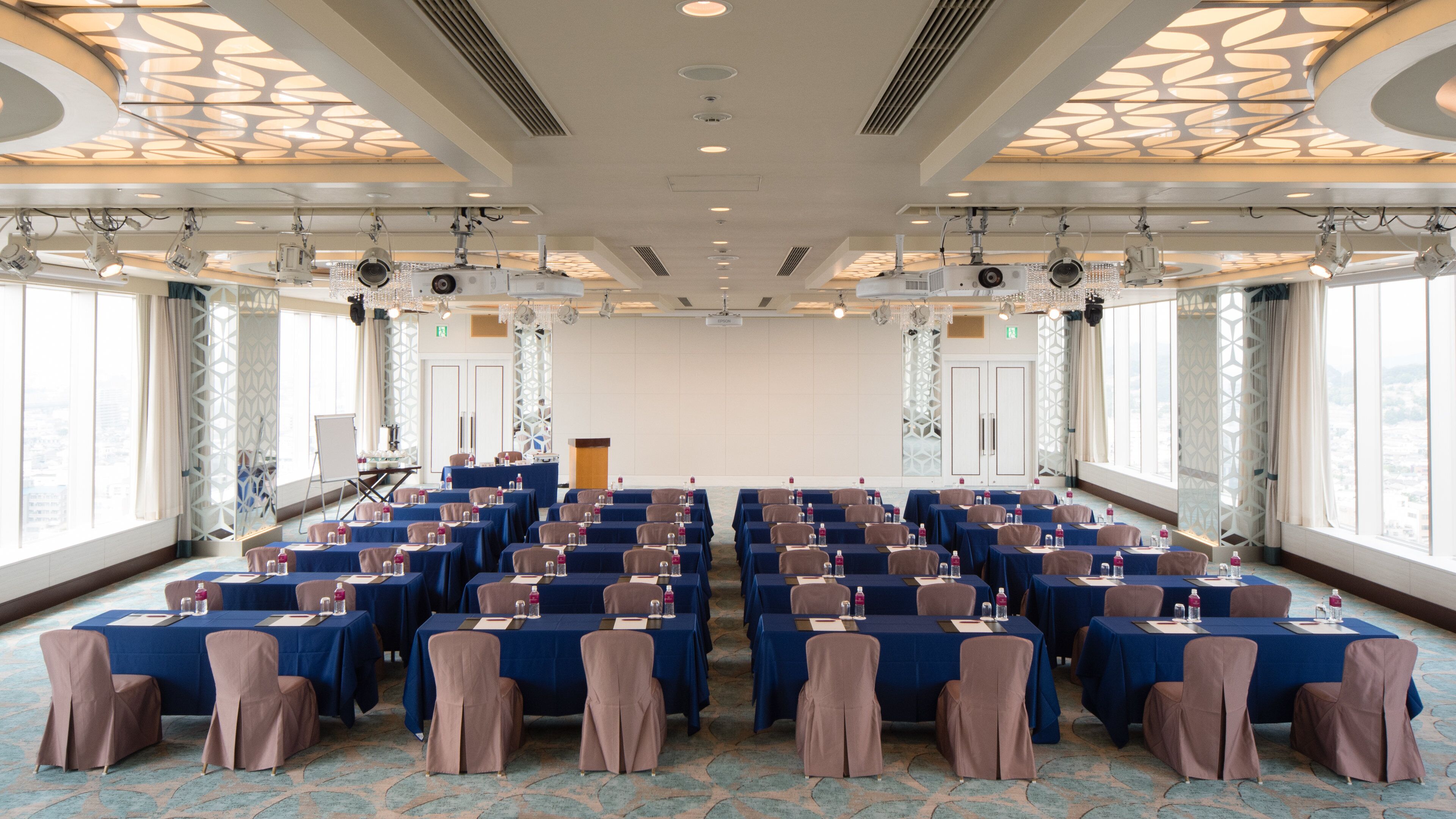 A conference room with rows of tables and chairs, large windows, and a podium.