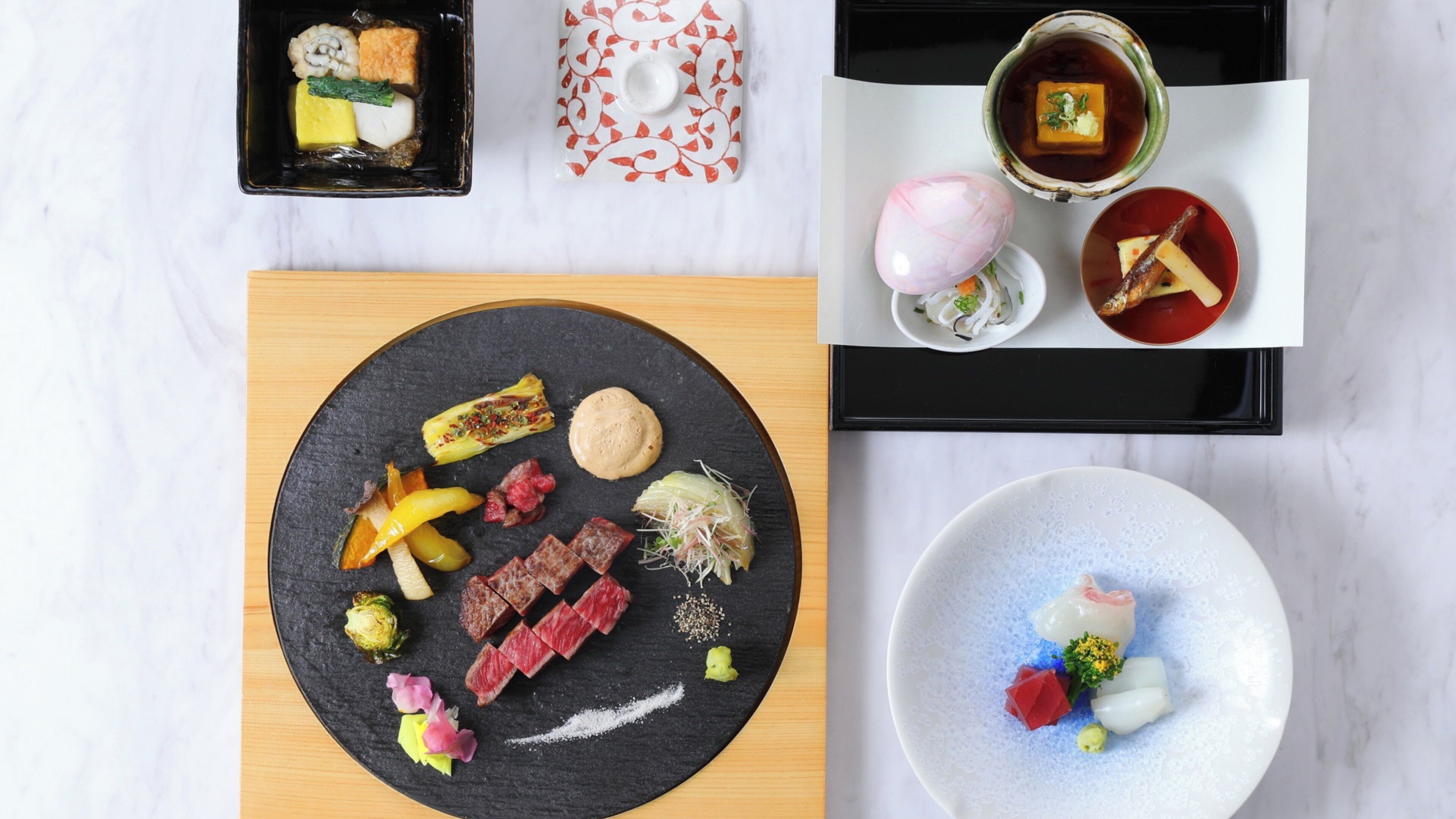 A variety of dishes on a table, including sushi, sashimi, and a meat dish, with a black plate in the center.