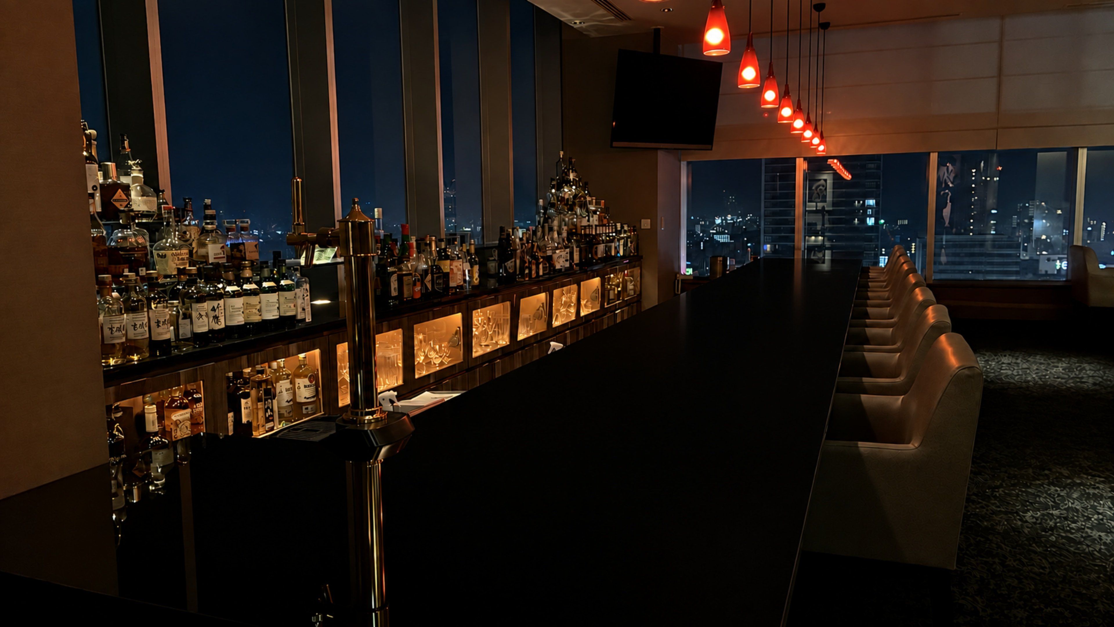 Een bar met uitzicht over de stad, flessen en een televisiescherm.