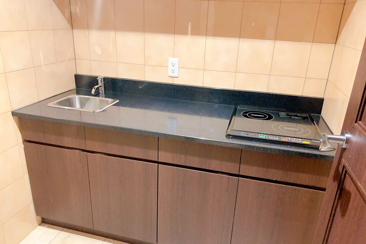 A compact kitchen with a black countertop, a stainless steel sink, and a built-in induction cooktop.