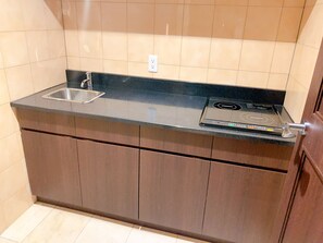 Una cocina compacta con encimera negra, un lavamanos de acero inoxidable y una placa de inducción integrada.