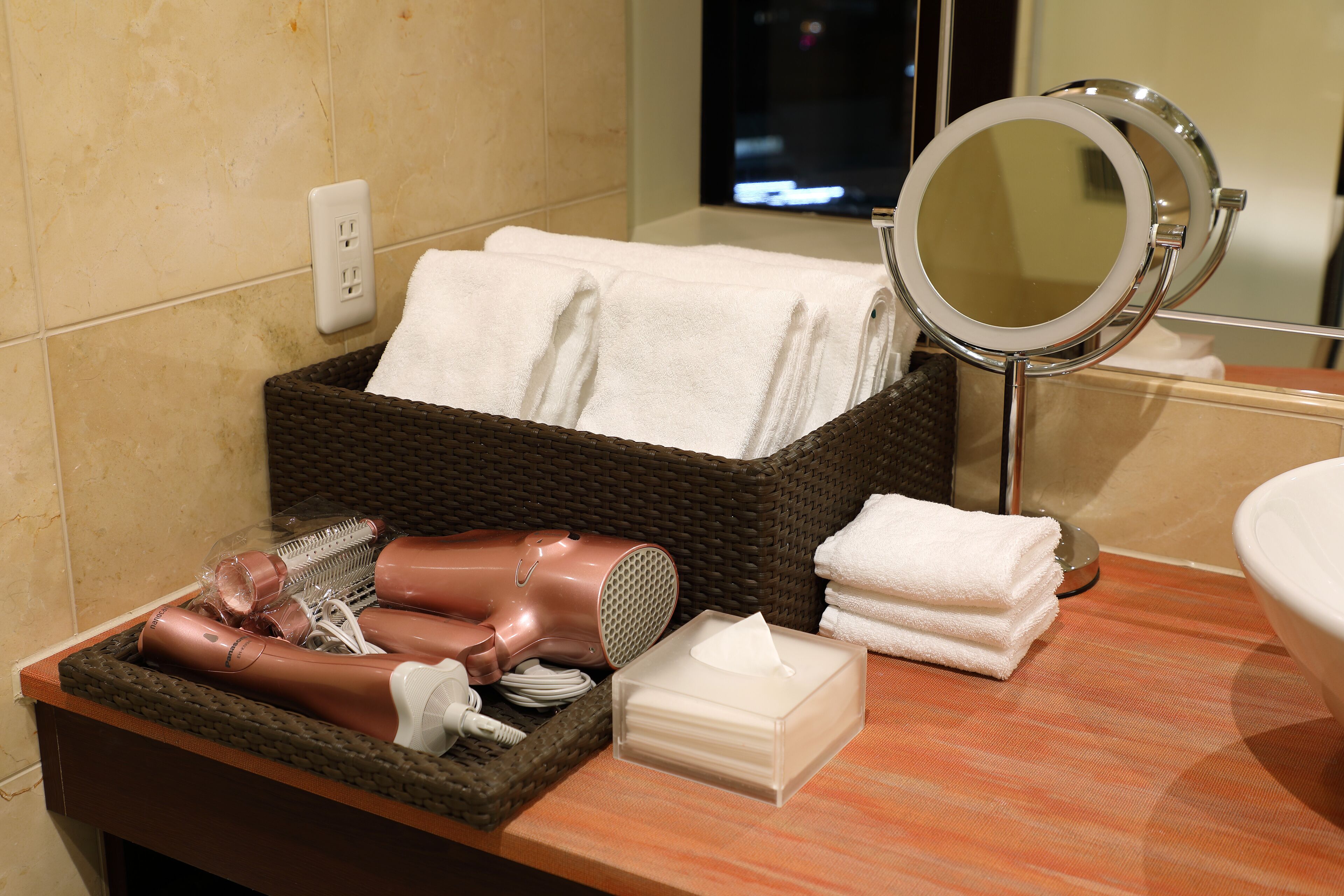A bathroom with a wicker basket containing towels, a hairdryer, and other toiletries.