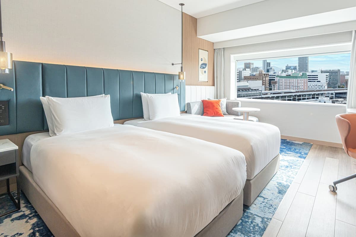 Une chambre d’hôtel avec deux lits, un bureau, une chaise, une vue sur la ville et un design moderne.