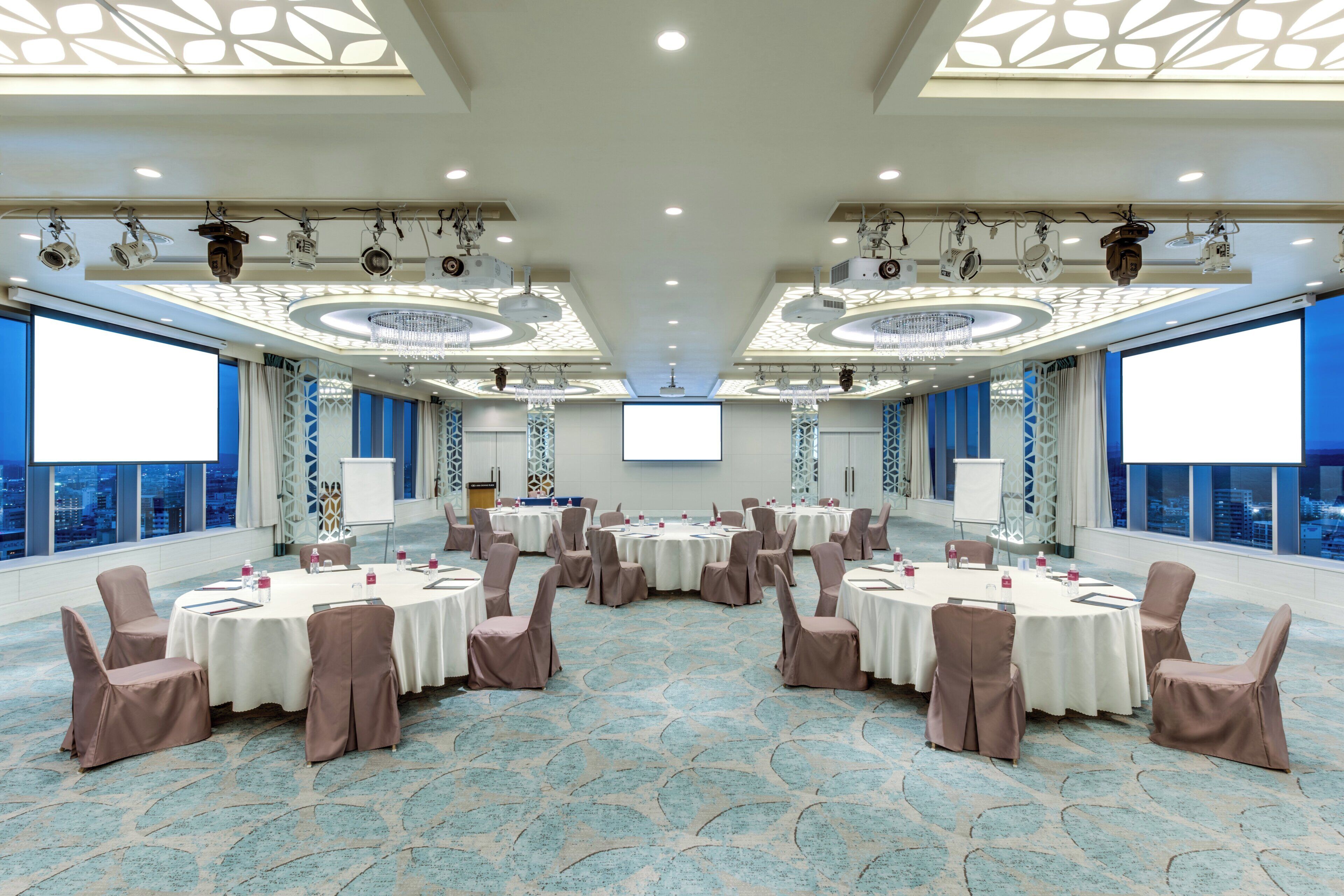 A conference room with round tables, chairs, a large screen, and city views.
