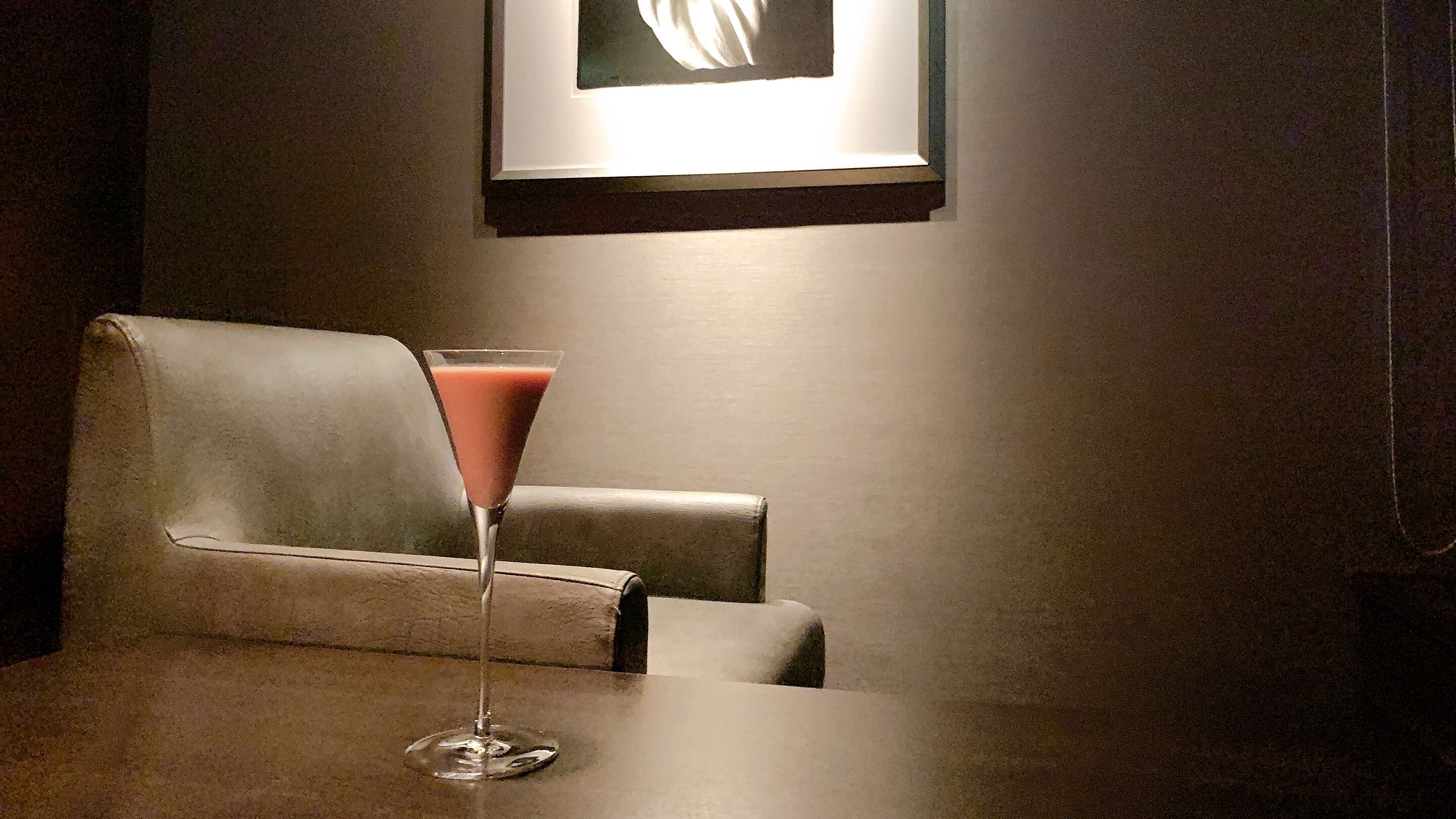 Et barområde med et enkelt cocktailglas på et bord, en læderarmstol og et indrammet billede på væggen.