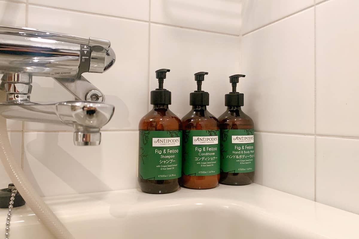 A bathroom with a chrome faucet and three bottles of Antipodes products on a white sink.