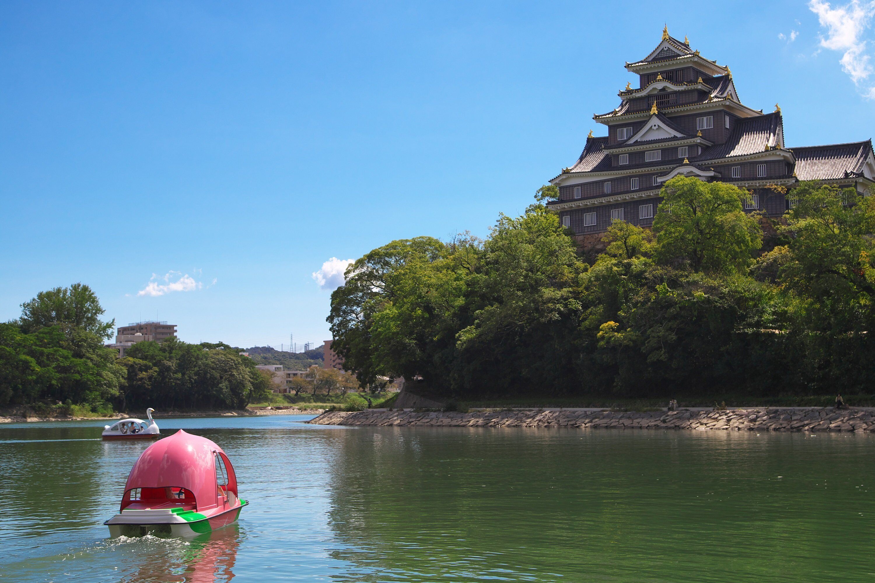Eine traditionelle japanische Burg an einem Fluss, im Vordergrund ein Boot.