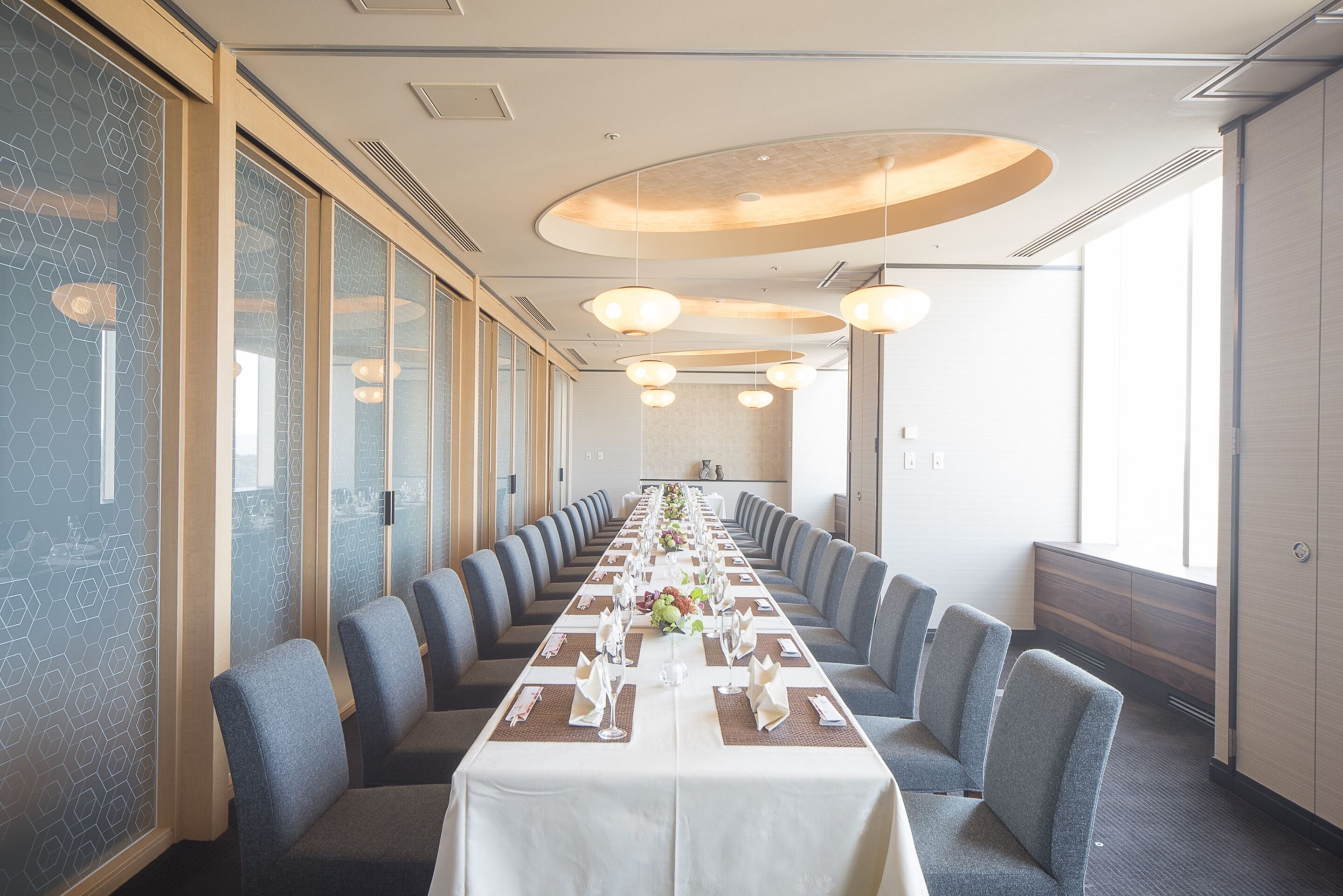Un salón de conferencias con una larga mesa dispuesta para una reunión, rodeado de sillas y grandes ventanales en un lateral.