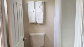 Une salle de bain avec des toilettes, deux serviettes accrochées au mur, une poubelle et un rideau de douche.