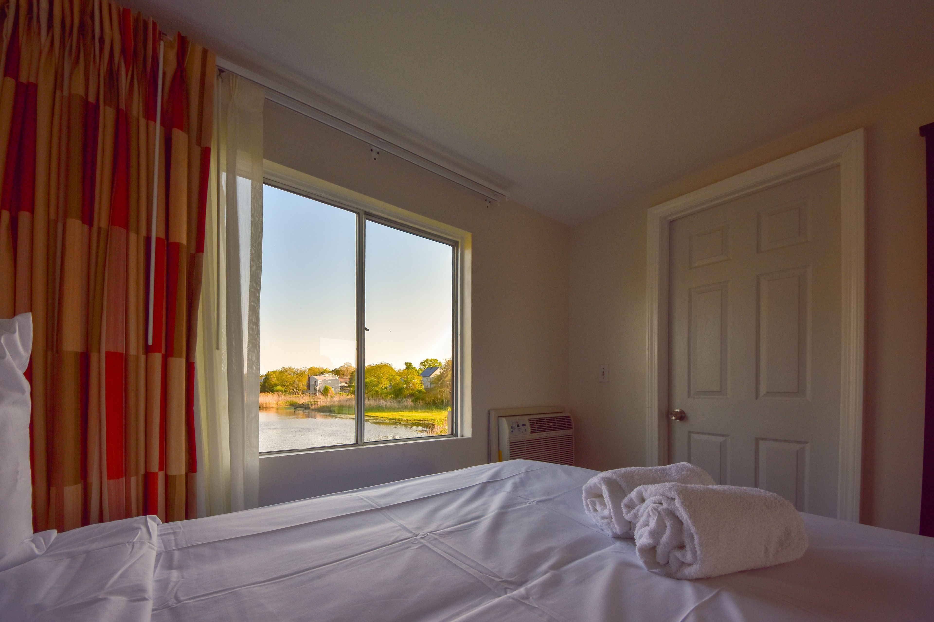 A hotel room with a large window, a bed with white linens, and a door.