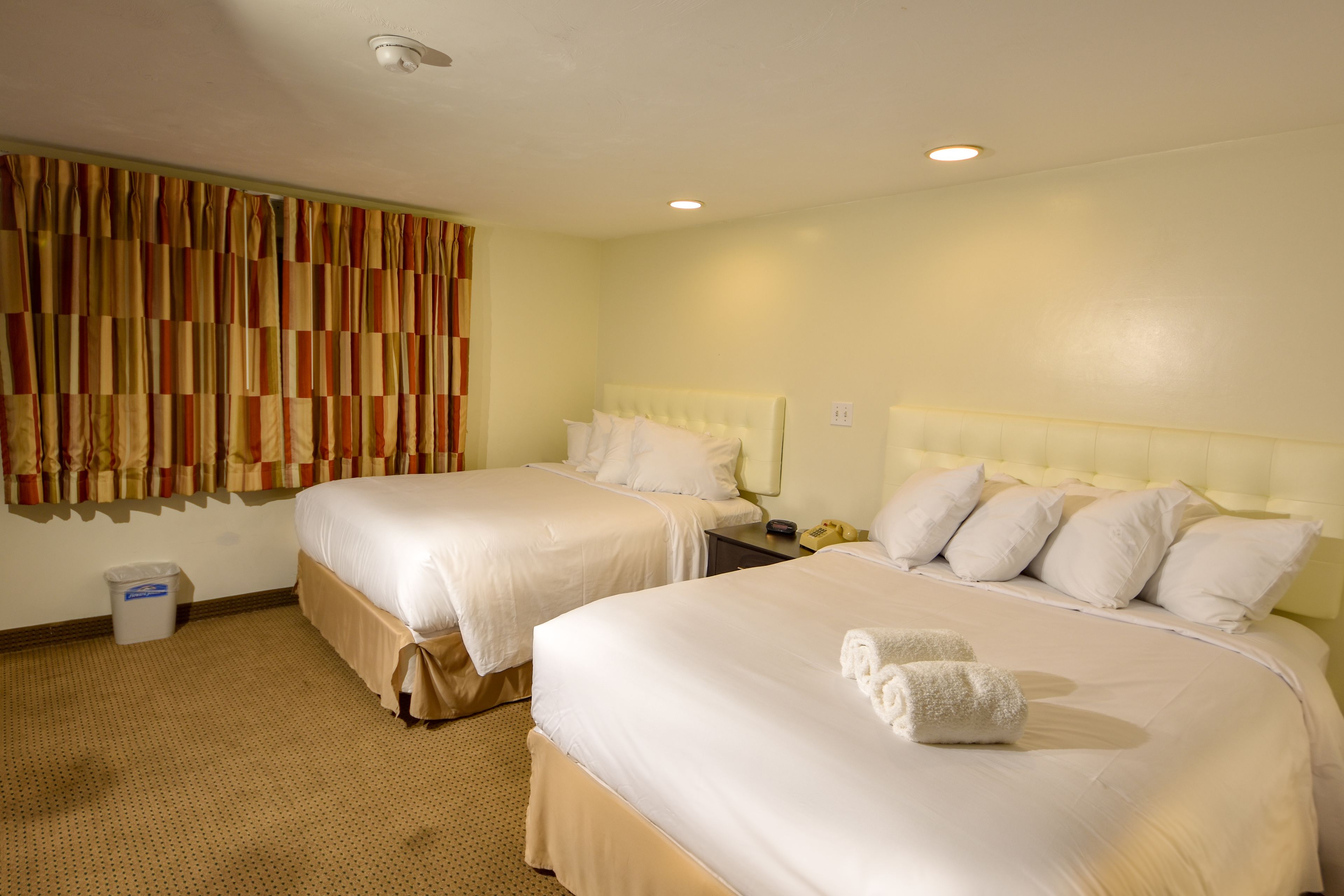 A hotel room with two beds, a waste bin, and a curtain.