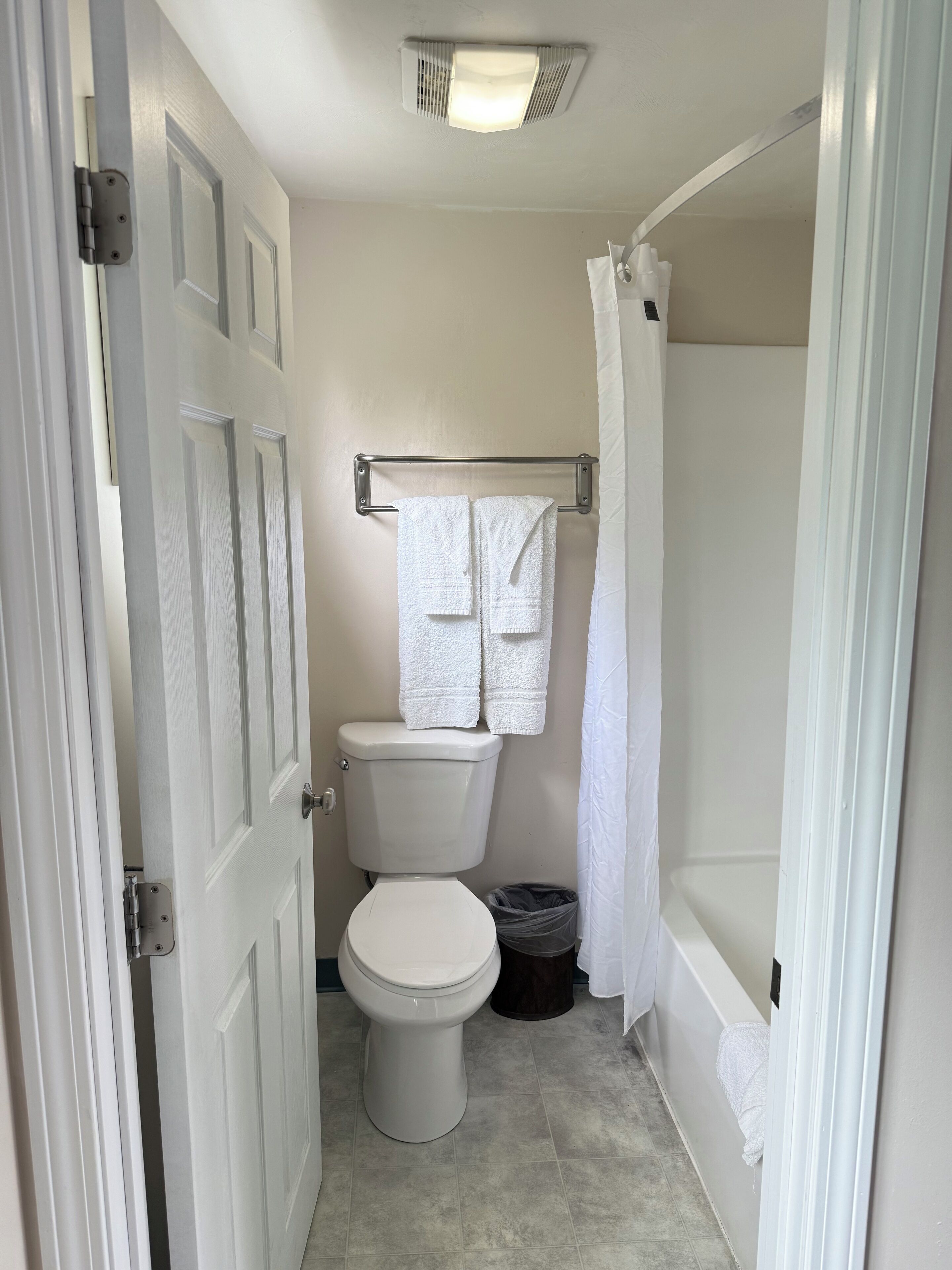 A small, clean bathroom with a toilet, a towel rack, a shower curtain, and a trash can.