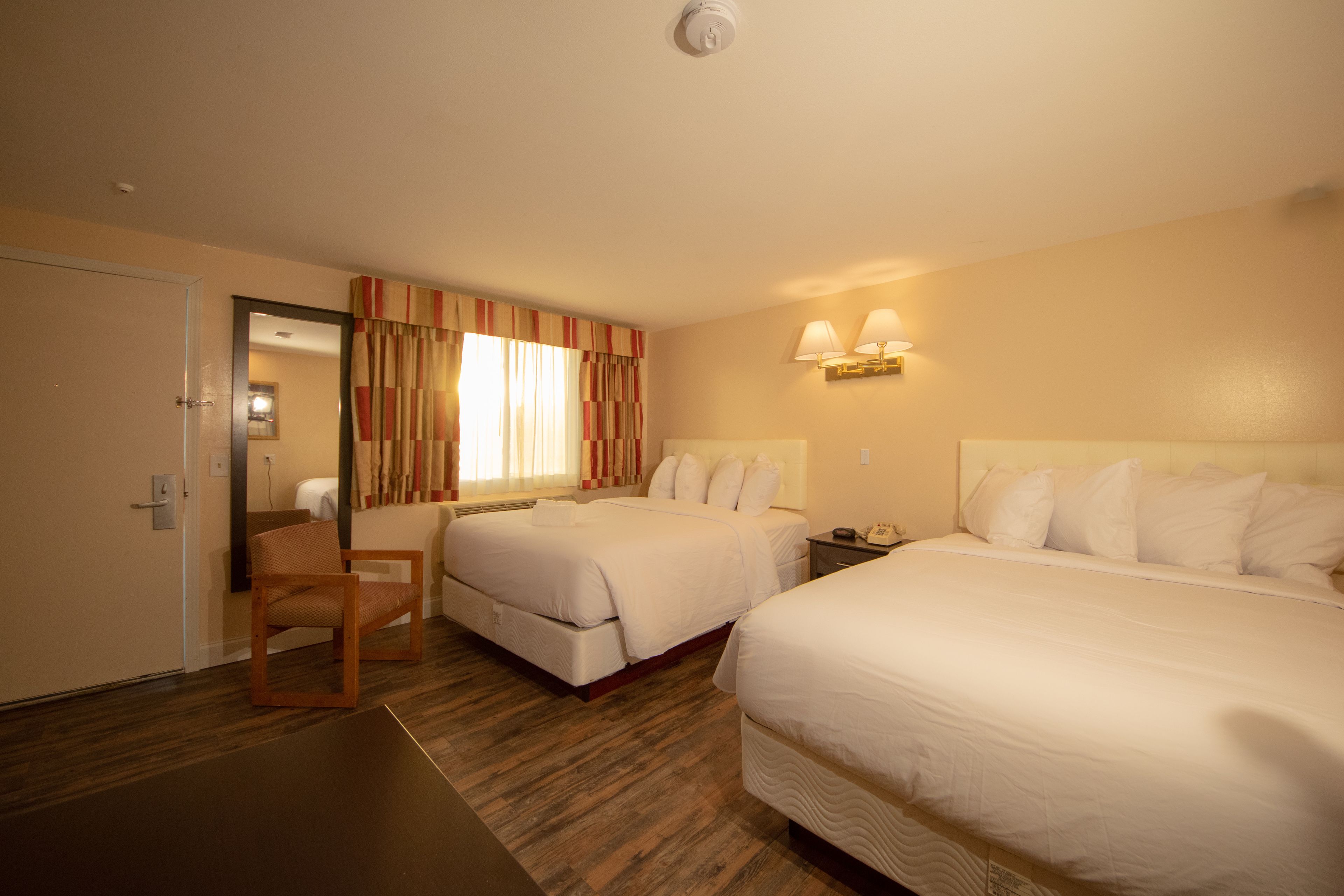Una habitación de hotel con dos camas, una silla de madera y una mesita de noche con una lámpara.