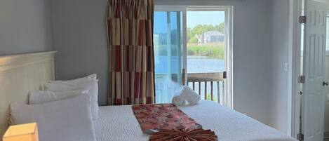 A hotel room with a large bed, a desk with a lamp, and a view of a body of water through a window.