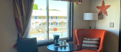 A hotel room with a window, a table with a coffee maker, two chairs, a lamp, and a star decoration on the wall.