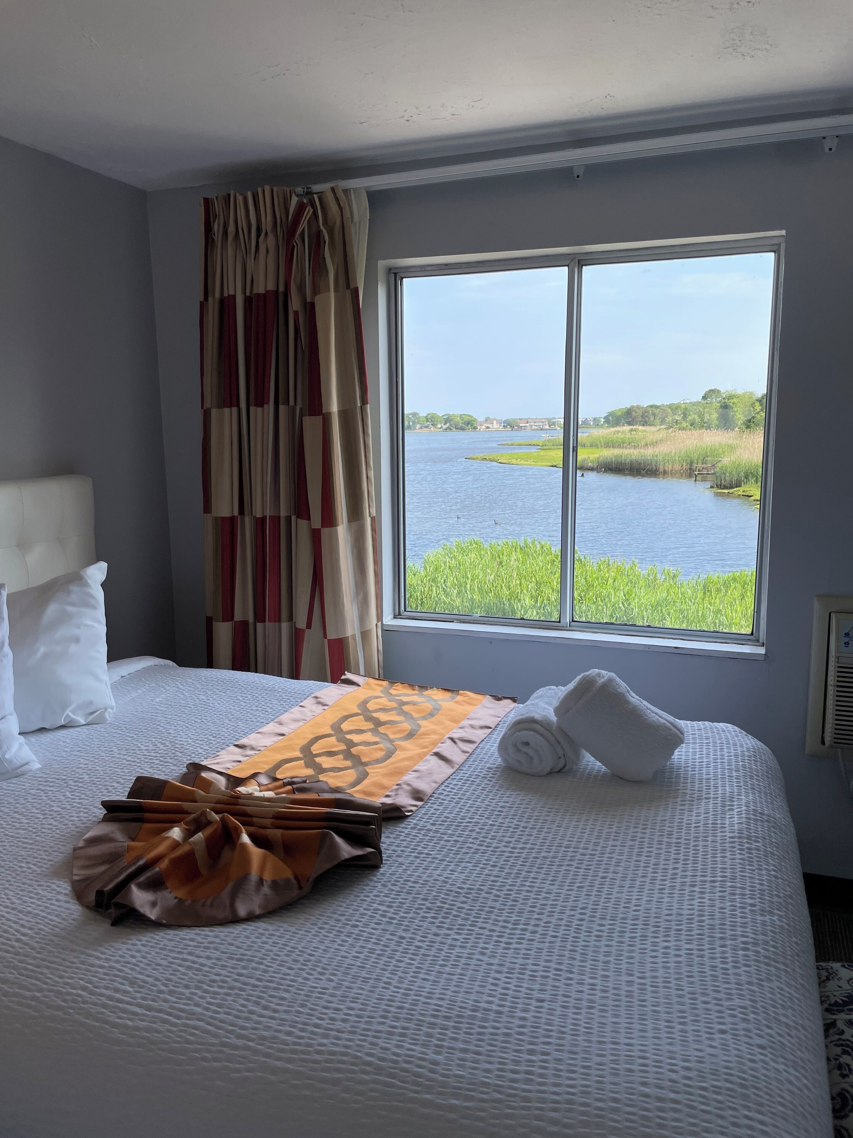 Habitación de hotel con un ventanal que ofrece vistas a un lago y follaje.