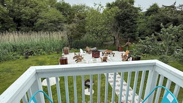 A deck with two turquoise chairs and a small table, overlooking a garden with a wooden table and chairs.