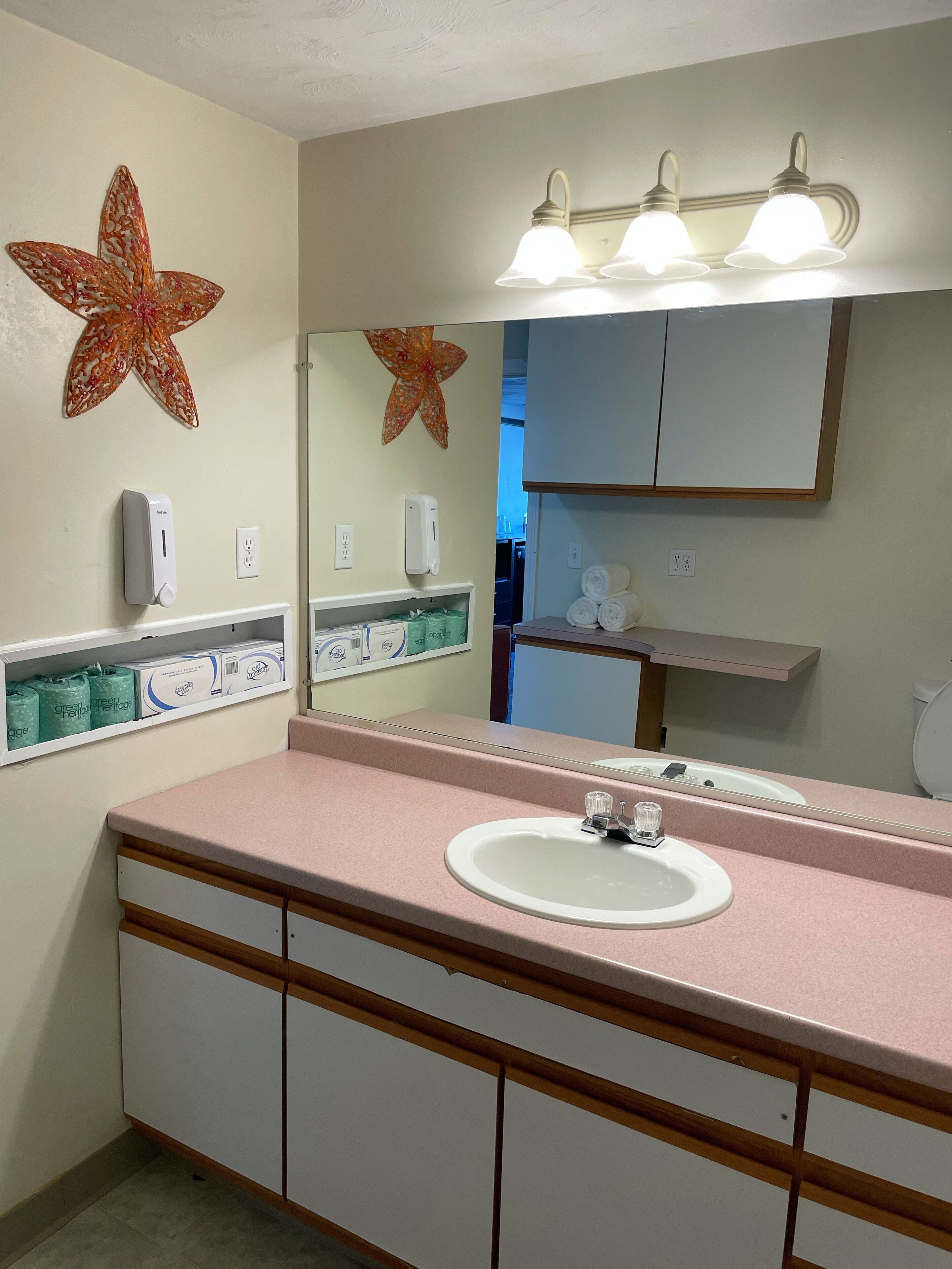 A bathroom with a pink countertop, a white sink, a mirror, and two starfish decorations.