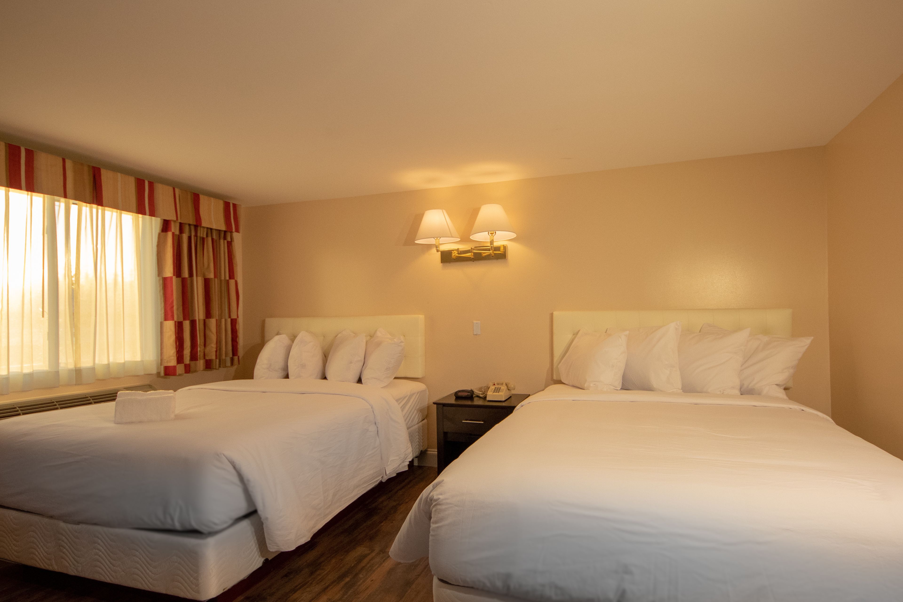 Habitación de hotel con dos camas, una mesita de noche, una lámpara y un ventanal con cortinas.