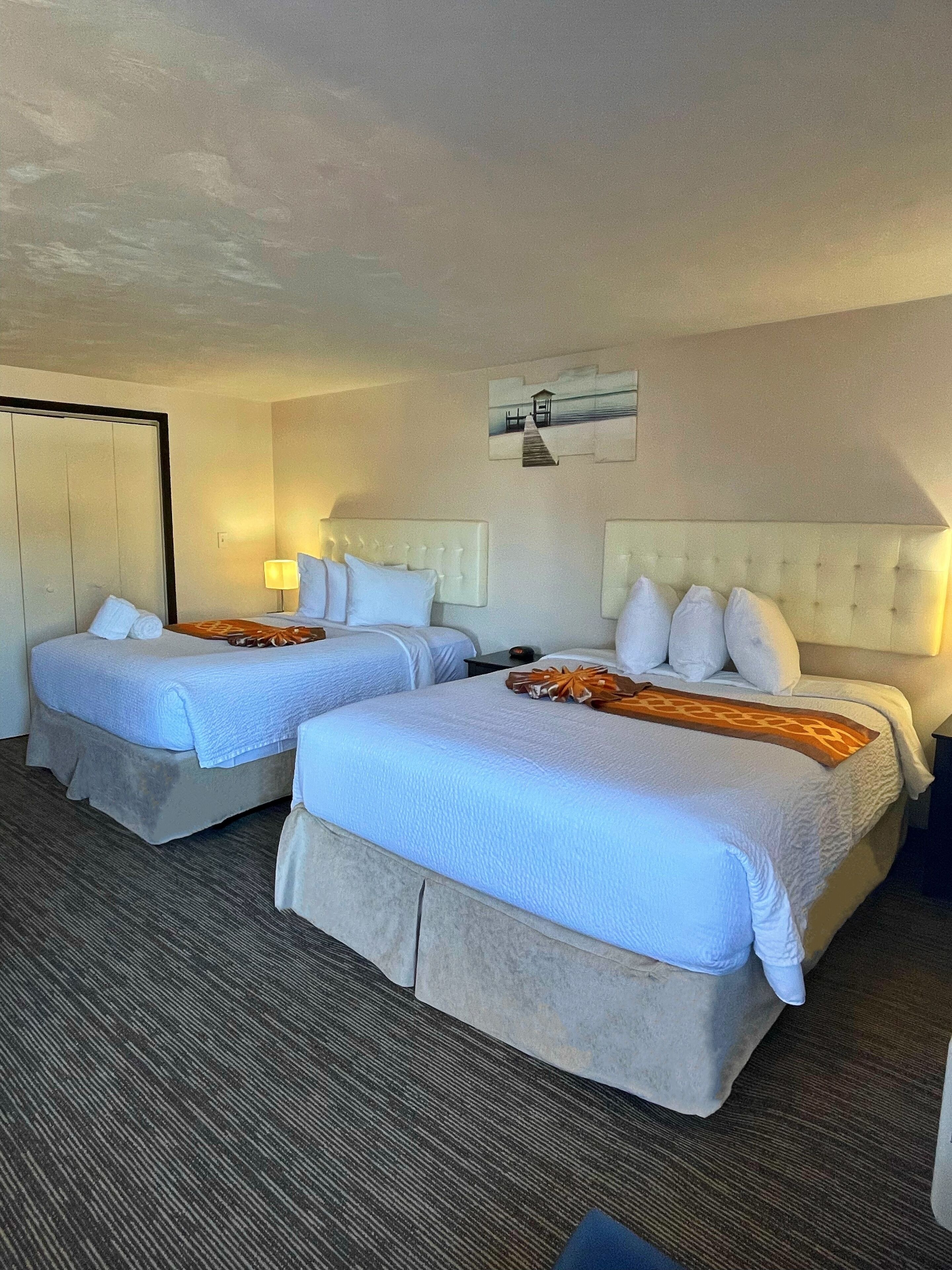 A hotel room with two beds, a wardrobe, a lamp, and a painting on the wall.