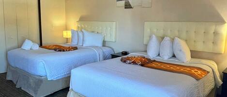 A hotel room with two beds, a wardrobe, a lamp, and a painting on the wall.