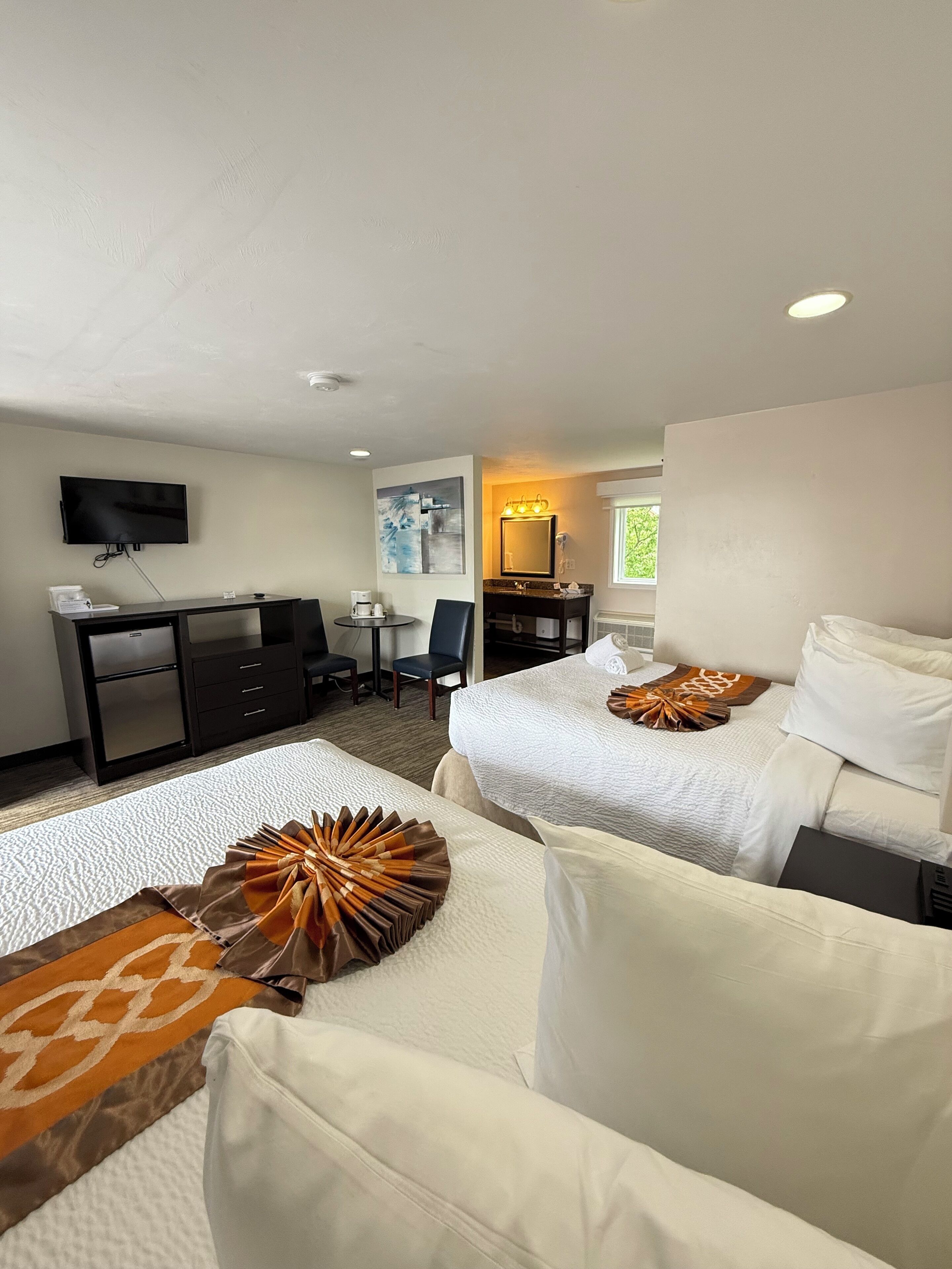 A hotel room with two beds, a desk, a television, and a bathroom.