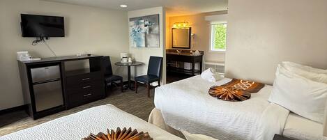 A hotel room with two beds, a desk, a television, and a bathroom.