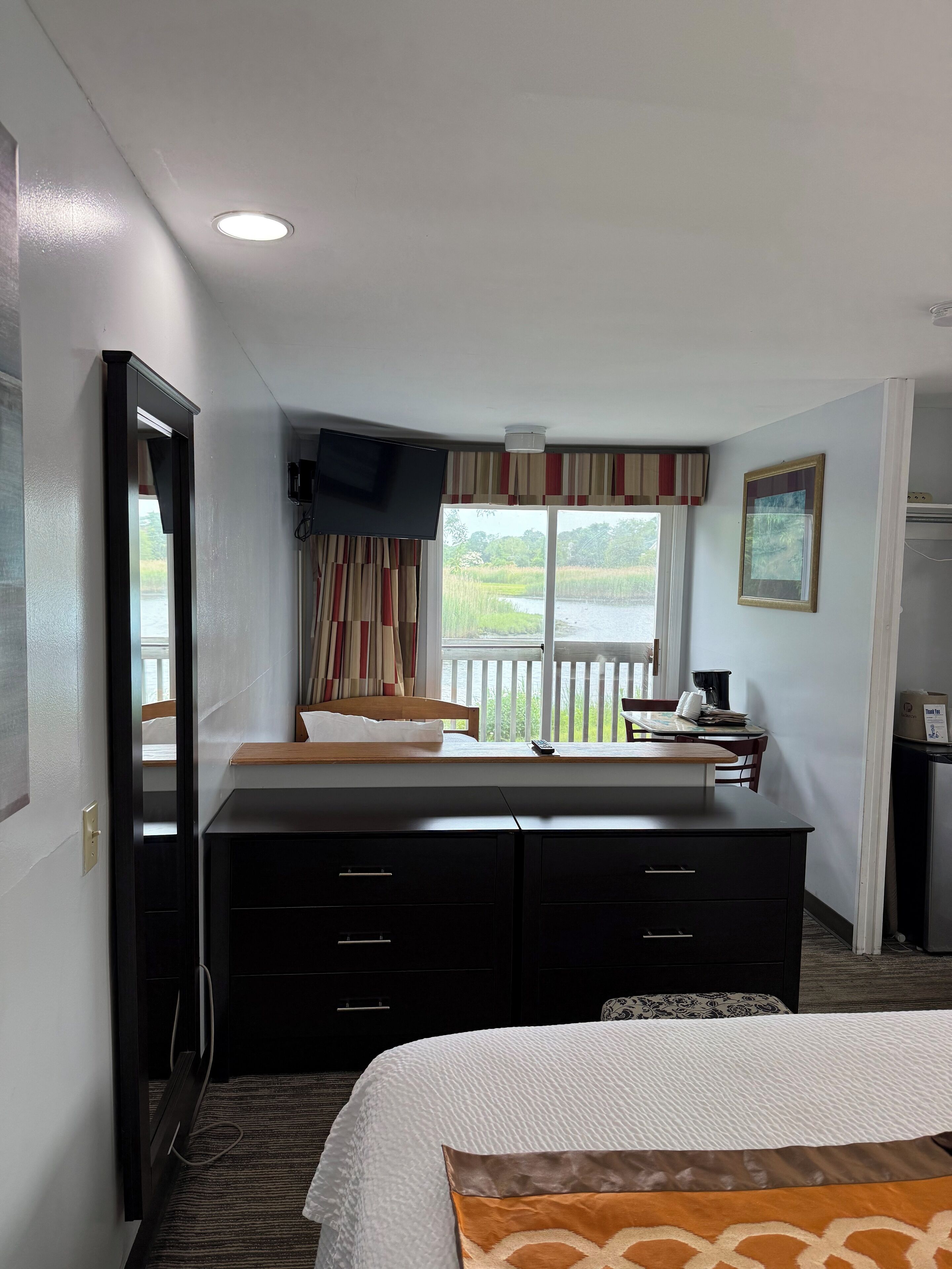 Habitación de hotel con cama, escritorio, silla, televisor y ventana con cortinas.