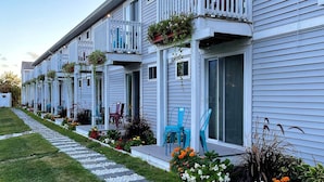 A row of white buildings with balconies, outdoor seating, and flower beds.