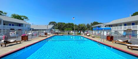 A rectangular swimming pool with a red border, surrounded by a fence, and adjacent to a building with a balcony.