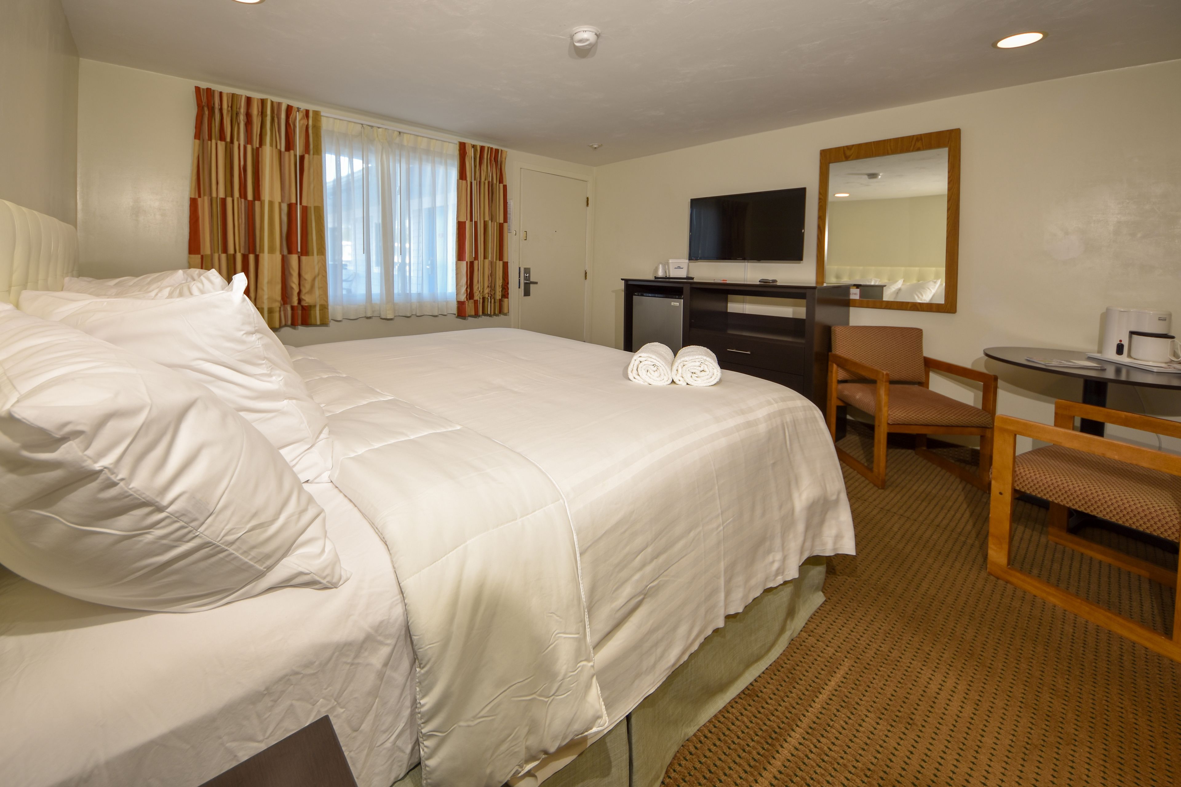 Een hotelkamer met een groot bed, een bureau, een stoel, een televisie en een spiegel.