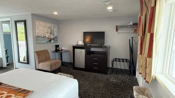 A hotel room with a bed, a desk with a TV, a chair, and a window with curtains.