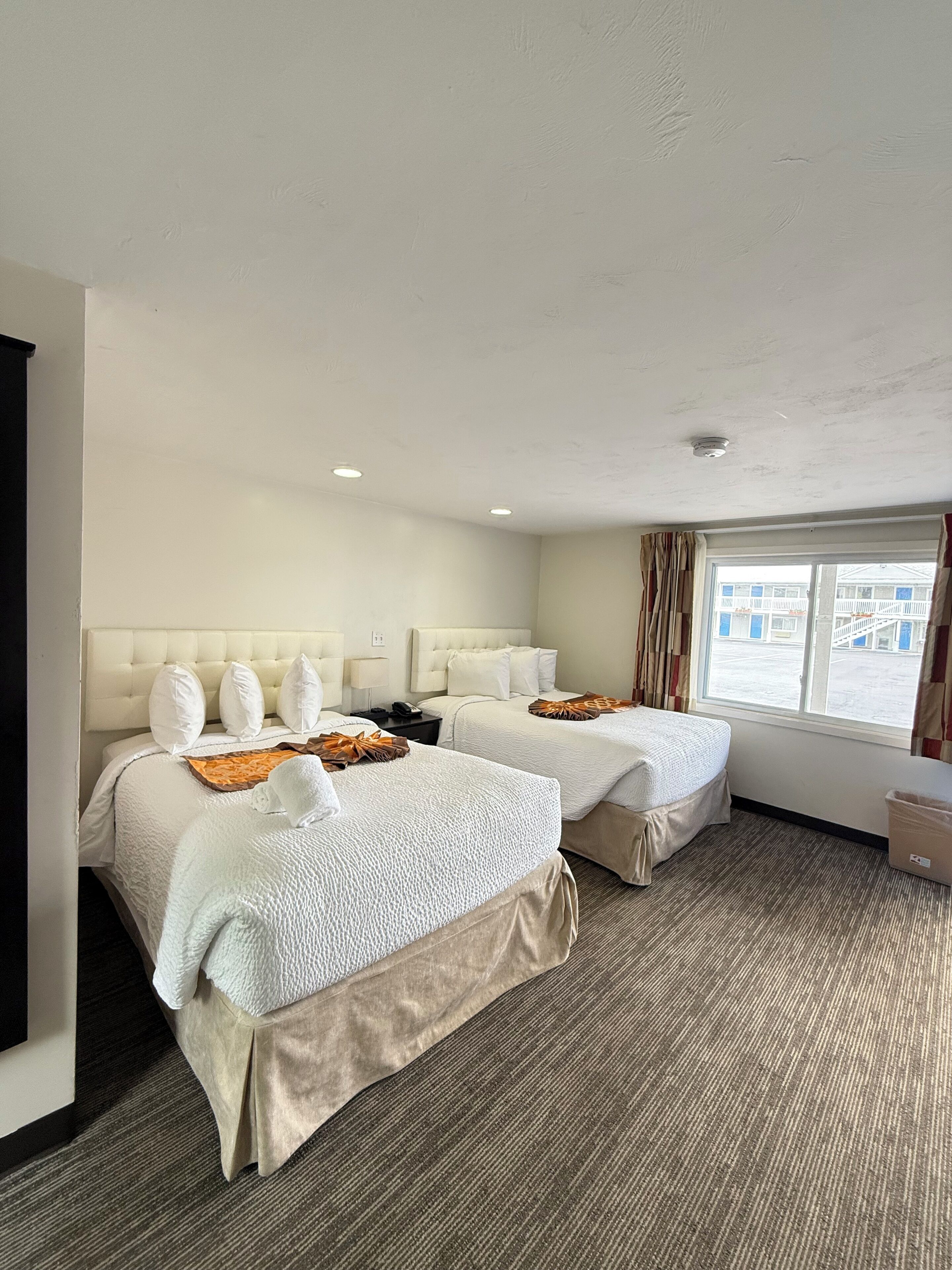 Ein Hotelzimmer mit zwei Betten, einem großen Fenster, einem Flachbildfernseher und einem Teppichboden.