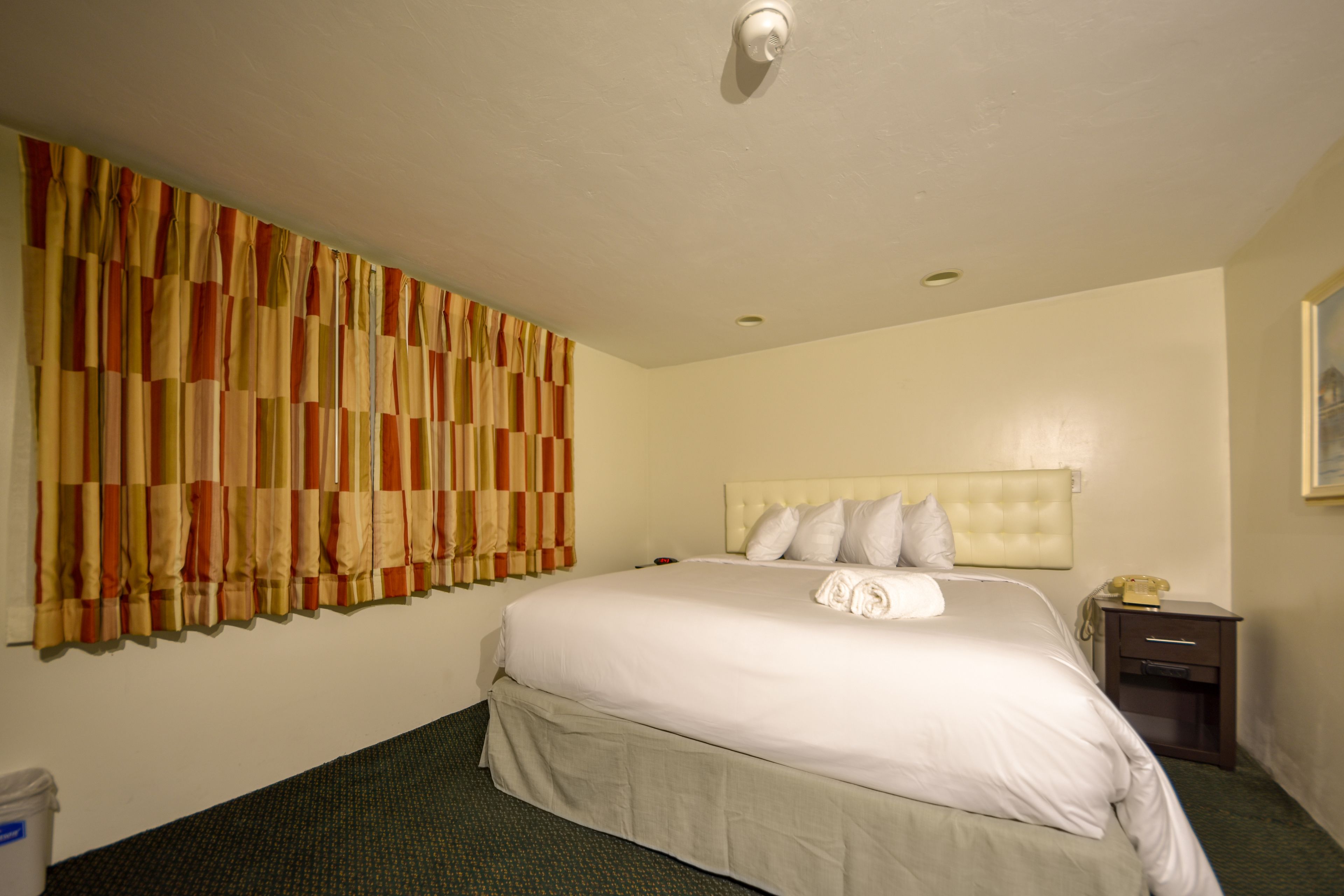 A hotel room with a large bed, a headboard, a nightstand, and a wall-mounted telephone.